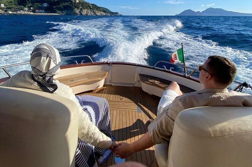 A boat on the sea with a flag, a person steering, and another person looking out. 1