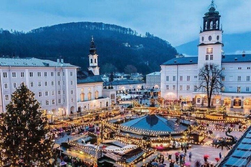 A festive square with illuminated decorations, a prominent clock tower, and surrounding buildings. 5