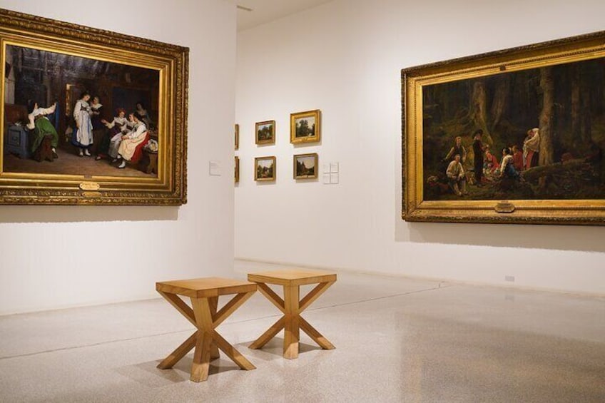 An art gallery with paintings on the walls and two wooden tables in the center. 5