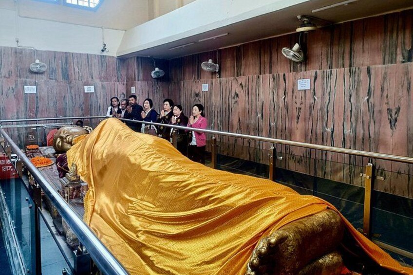 A golden statue covered with a cloth, surrounded by a railing, in a room with marble walls and ceiling fans. 4