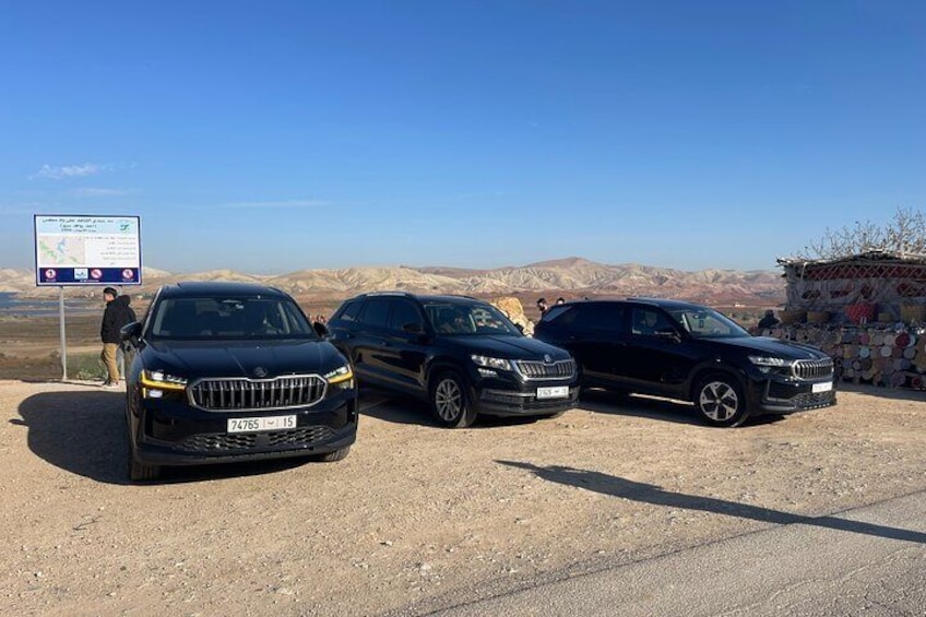 Tres SUVs negros estacionados en un camino de tierra con un cartel de señalización al fondo y un paisaje montañoso. 4
