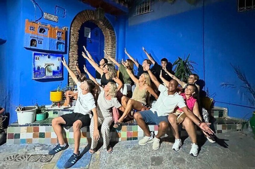 Un grupo de personas sentadas en escalones de un edificio de paredes azules con piso de baldosas y una ventana circular. 1
