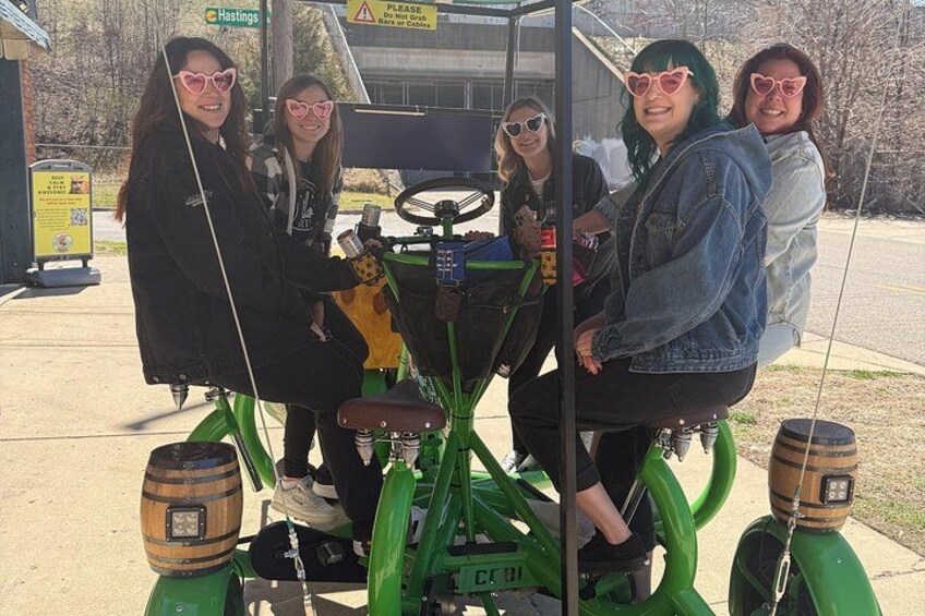 Four people on a green tractor with a trailer, parked on a paved area. 2