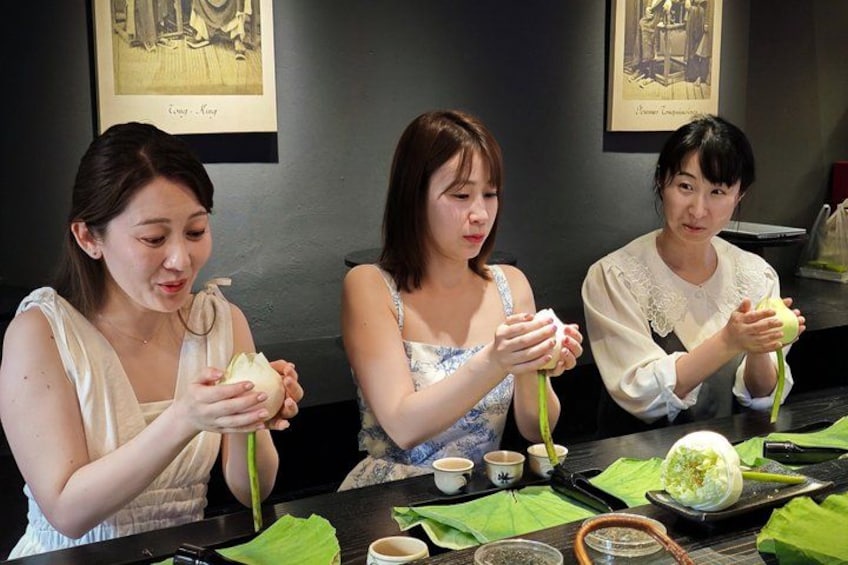 Tre persone che preparano cibo a tavola con bacchette, ciotole e una foglia verde. 3