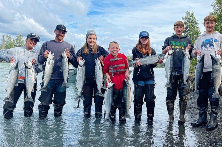 Seven people standing in a river holding fish. 1