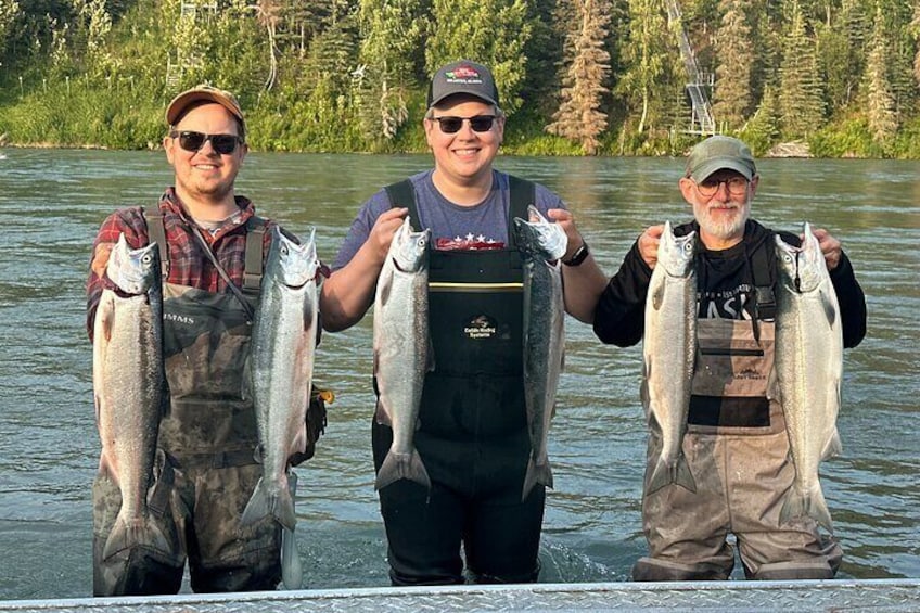 Three people holding fish in a river. 3