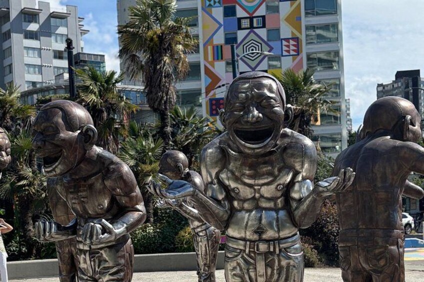 Un grupo de esculturas metálicas en un entorno urbano, con edificios y palmeras al fondo. 1