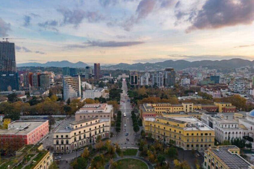 Un paisaje urbano con un bulevar central, edificios y montañas al fondo. 3