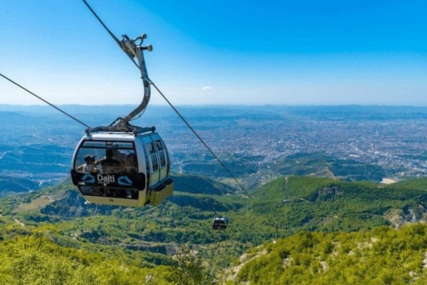 Una funivia con marchio 'Delfi', sospesa da cavi, che domina una città e un paesaggio collinare. 1