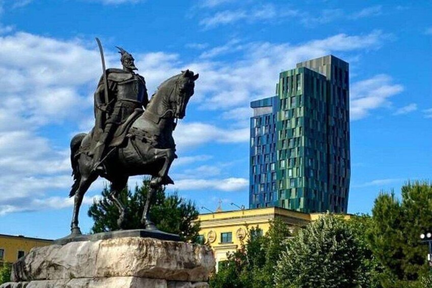 Una estatua de una figura a caballo, un edificio moderno y un cielo azul despejado. 5