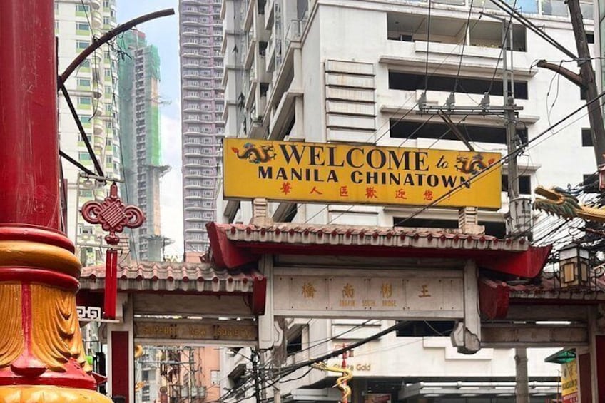 Skilt der byder besøgende velkommen til Manila Chinatown, med traditionelle kinesiske arkitektoniske detaljer og en travl gade i baggrunden. 4
