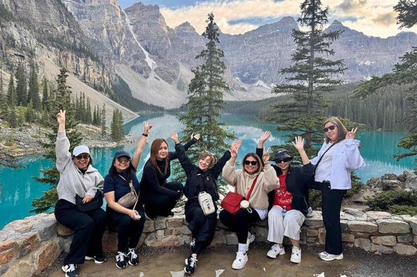A group of people posing by a lake with mountains in the background. 1