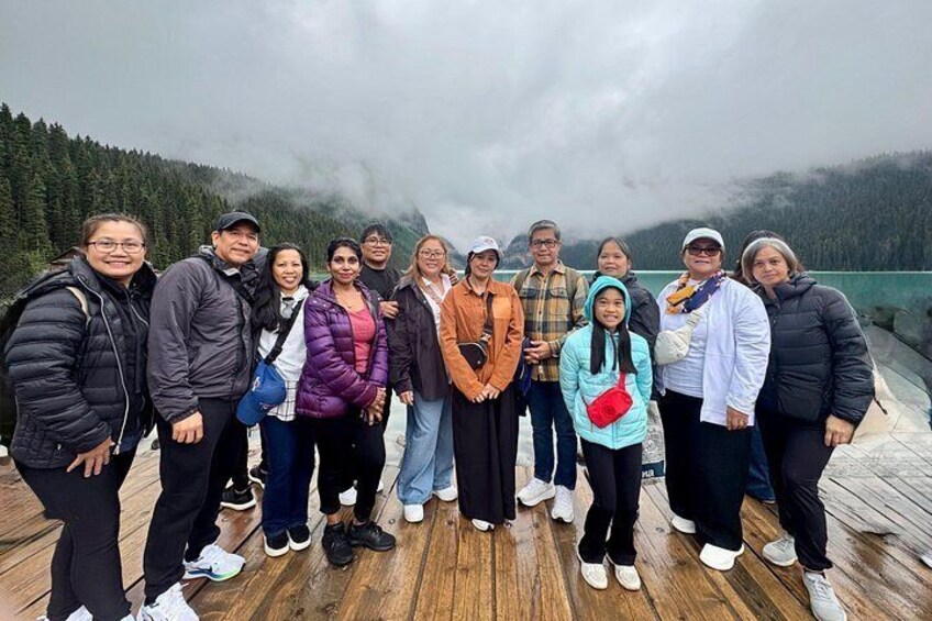 A group of people standing on a wooden deck with a forested mountain backdrop. 3