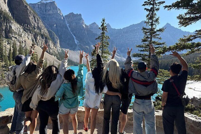A group of people standing on a rocky ledge, facing a mountainous landscape with a lake. 5