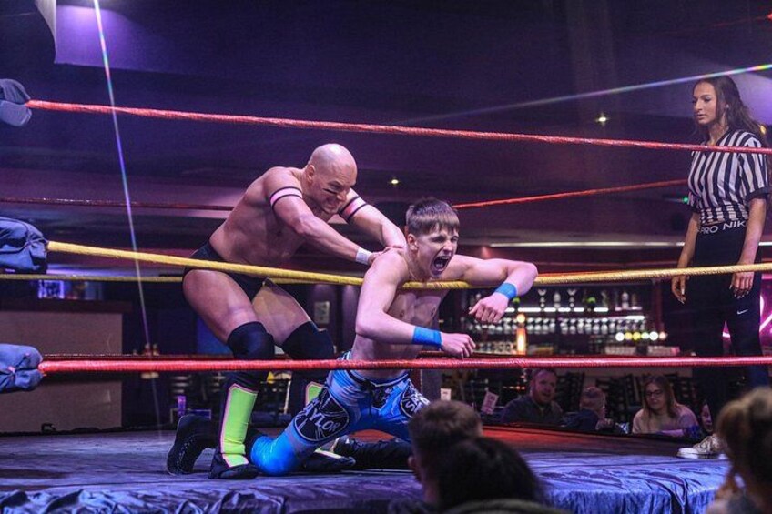A wrestling match in a ring with ropes, a referee, and an audience. 5