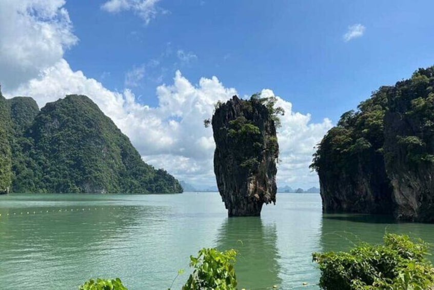 A large rock formation in a body of water surrounded by lush green hills. 1