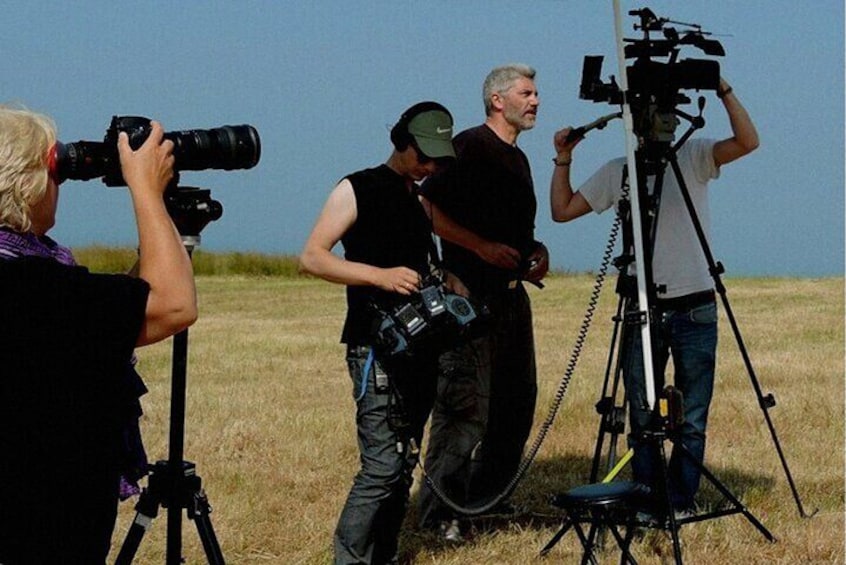 A group of people with cameras and a large camera on a tripod in an open field. 5