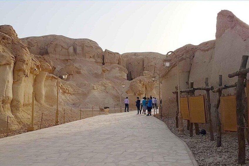 A pathway in a desert with large rock formations and wooden barriers. 1