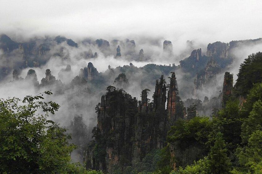 Un paisaje montañoso cubierto de niebla, con imponentes formaciones rocosas y vegetación densa. 2