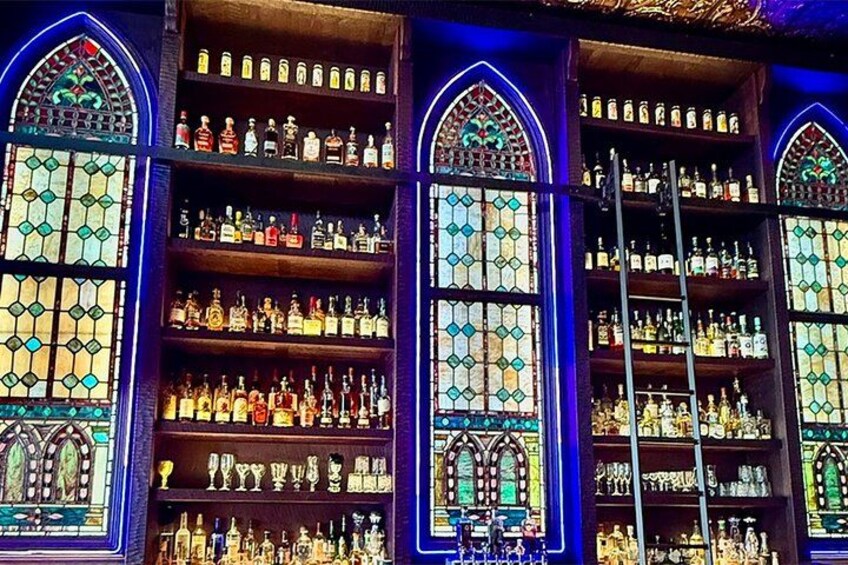 Eine Bar mit Buntglasfenstern und Regalen voller Spirituosenflaschen. 1