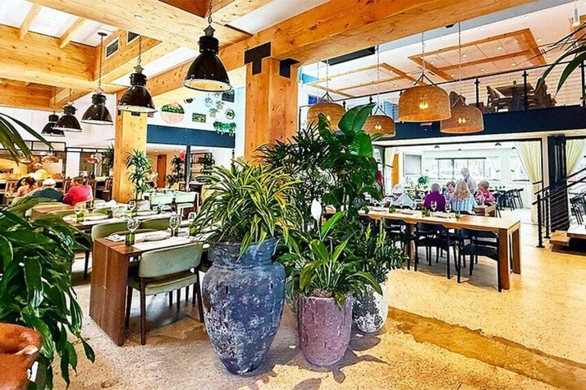 Een ruime eetruimte met houten balken, grote potplanten en hangende hanglampen. 3