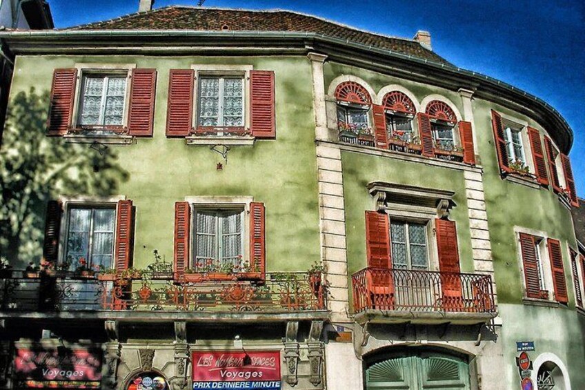 A green building with red shutters, a sign reading 'Les Voyages,' and a balcony with railings. 2