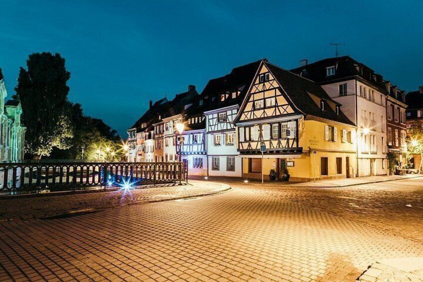 A cobblestone square with traditional half-timbered buildings, a bridge, and a tree in the background. 2