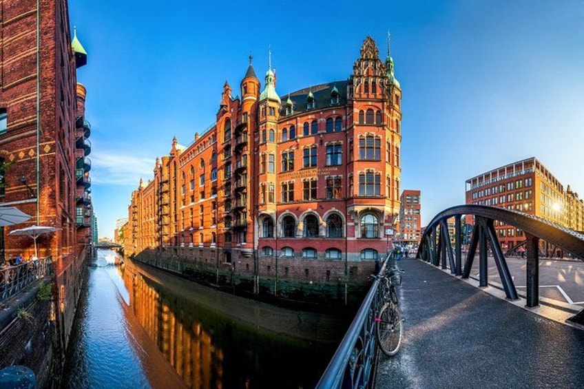 A canal with a bridge, a large red brick building with a green dome, and a reflection in the water. 4