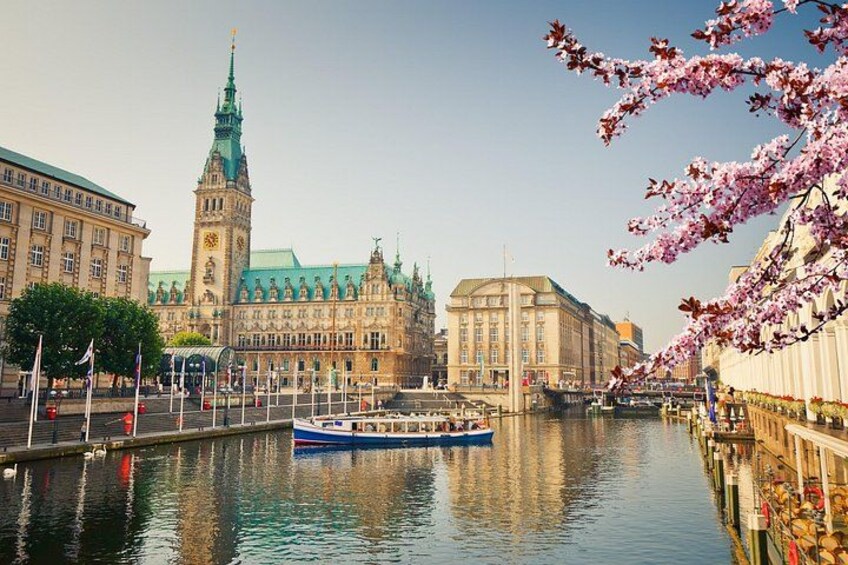A river with a boat, a large building with a clock tower, and cherry blossoms. 5