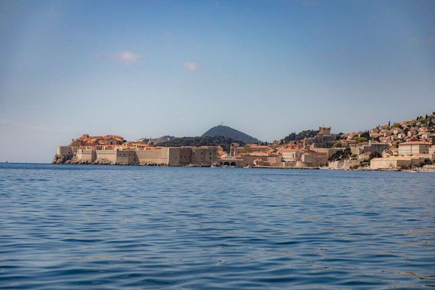 A coastal town with historic buildings, a prominent hill in the background, and calm sea. 4
