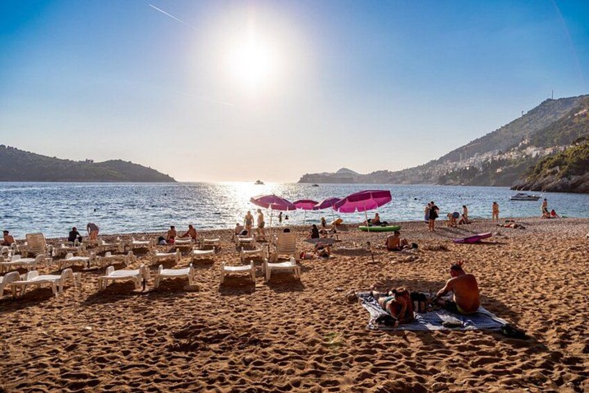 A beach with sunbathers, umbrellas, and boats on the water. 1