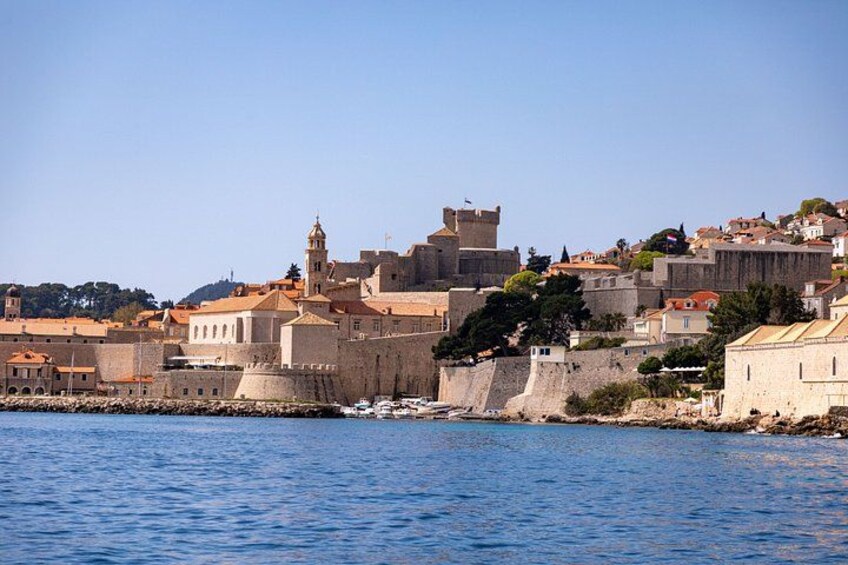 A coastal cityscape with historic buildings, a prominent tower, and a fortified wall. 2