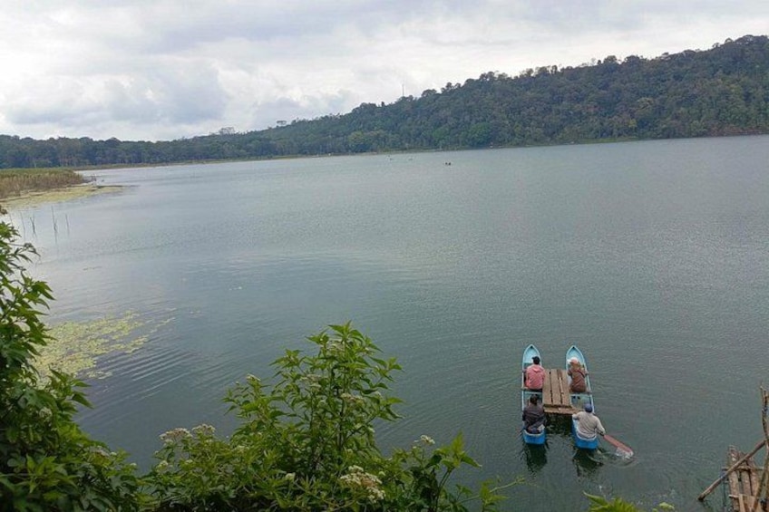 Un lago tranquilo con dos barcos anclados cerca de la orilla, rodeado de vegetación y un paisaje montañoso al fondo. 2