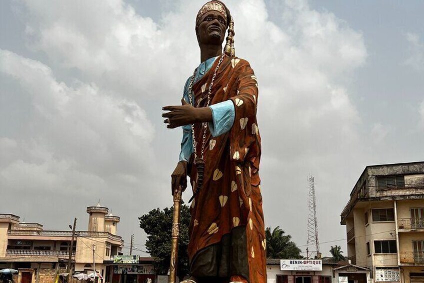 Eine Statue einer Person in traditioneller Tracht mit blauem Hemd und braunem Gewand mit Blattmustern. 5