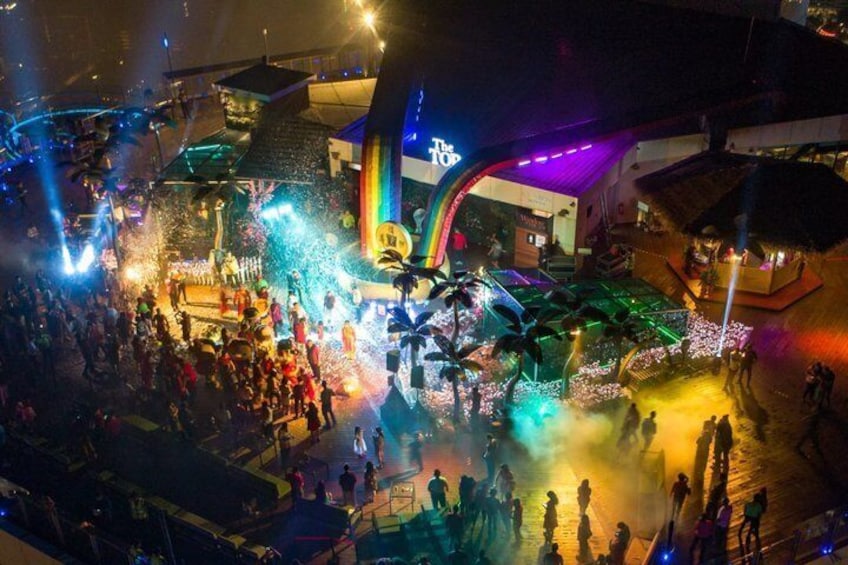Ein lebhaftes Open-Air-Event mit Bühne, Palmen und einer farbenfrohen Struktur. 3