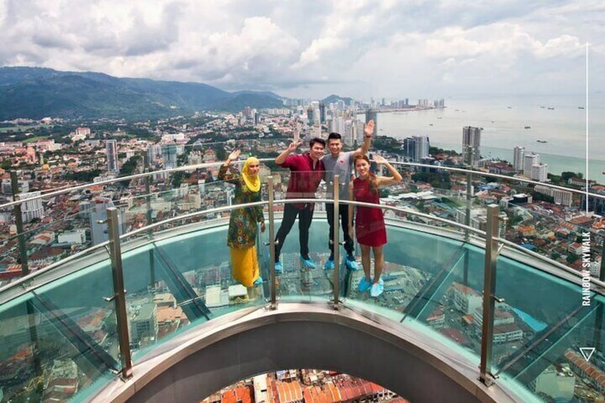 Eine Gruppe von Menschen steht auf einer Glasbrücke, im Hintergrund eine Stadtlandschaft und Berge. 1