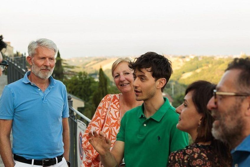 A group of people standing on a balcony overlooking a landscape with hills and trees. 3