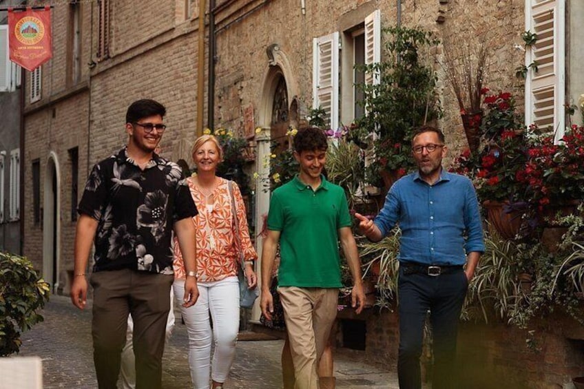 A group of people walking on a cobblestone street with brick buildings and potted plants. 5