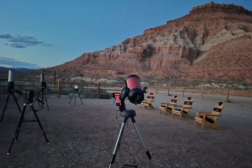 A telescope on a tripod, several chairs, and a desert landscape with a mountain in the background. 3