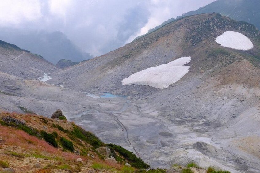 A mountainous landscape with snow patches, a glacier, and a rocky terrain. 2