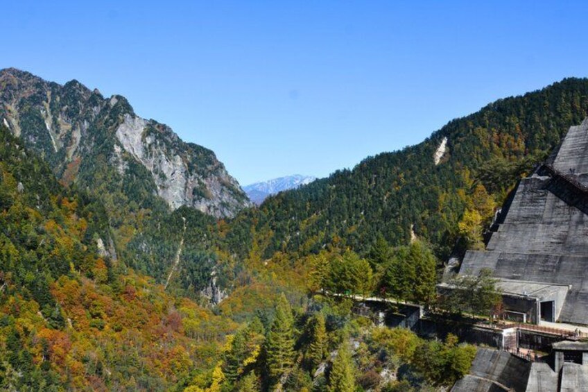 Paisaje montañoso con follaje otoñal, una gran estructura de presa y cielo despejado. 2