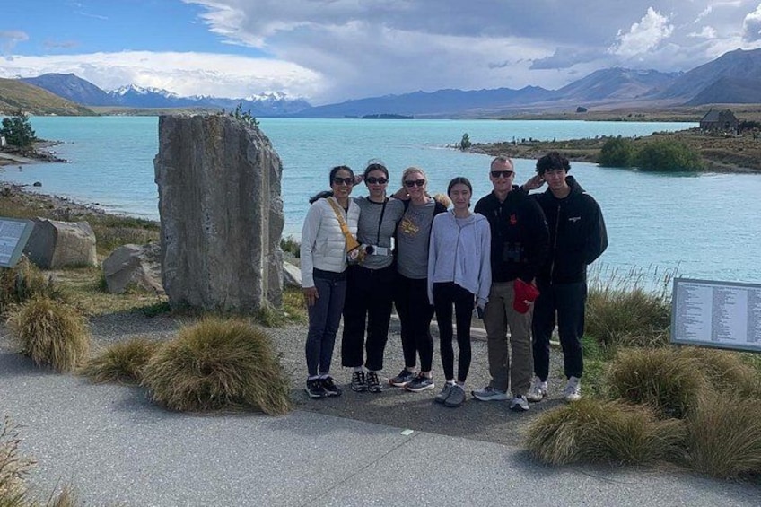 A group of people standing by a lake with mountains in the background. 3