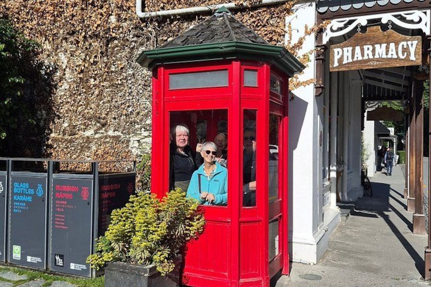 Eine rote Telefonzelle mit einer Person darin, ein Apothekenschild und Glascontainer. 3
