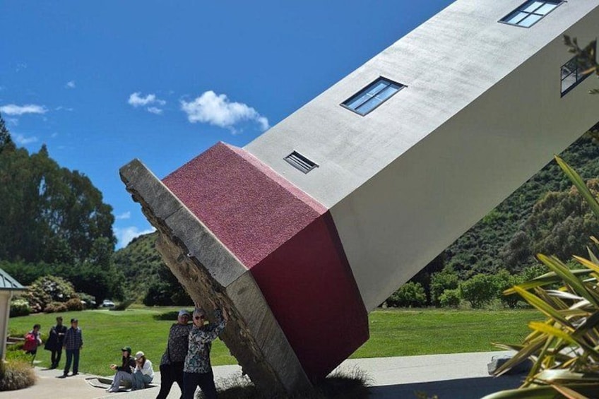 A tilted building with a red and white facade, surrounded by greenery and a clear sky. 2
