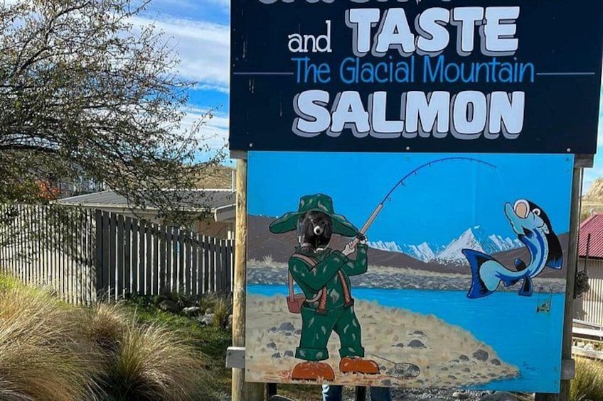 Schild mit Werbung für Glacial Mountain Salmon, mit einem Cartoon-Fischer und einem Lachs. 5