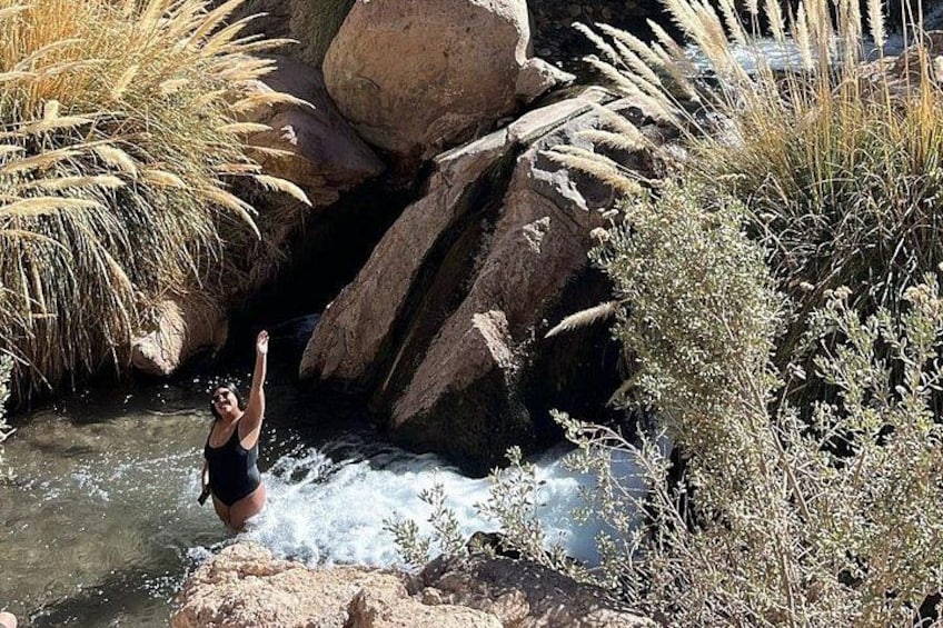 Una persona saltando a un río rodeado de rocas y pasto seco. 3