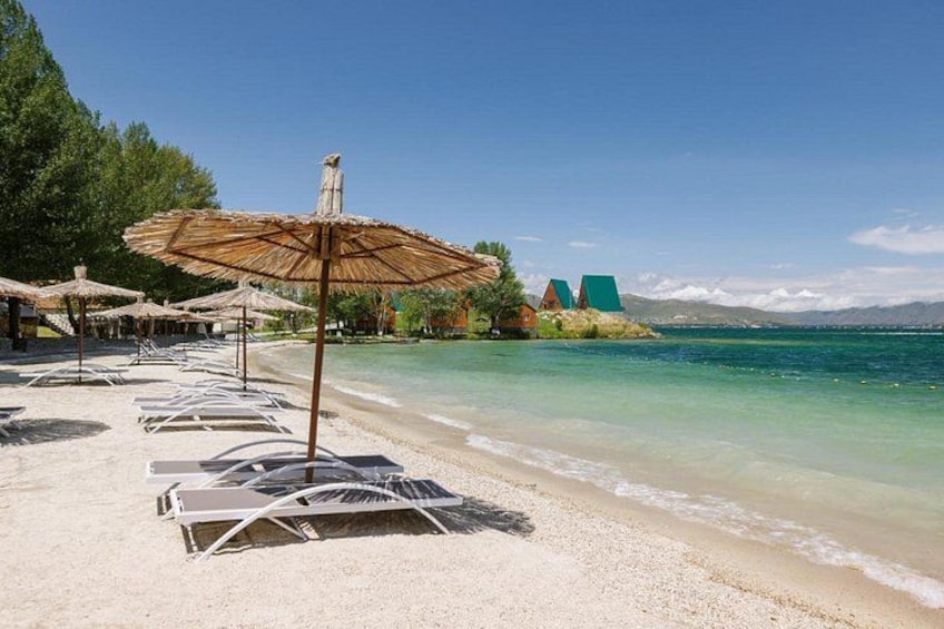 Een strand met ligbedden en parasols, een helderblauwe lucht en een bergachtige achtergrond. 1