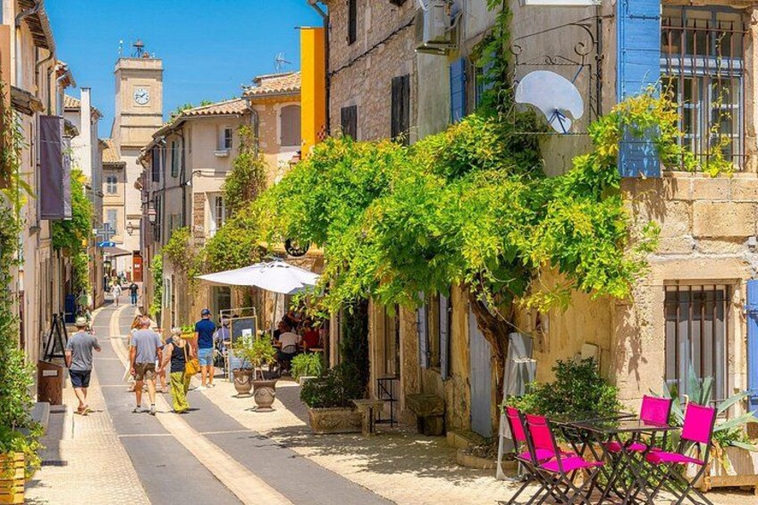 A narrow street lined with buildings, a clock tower, and people walking. 3