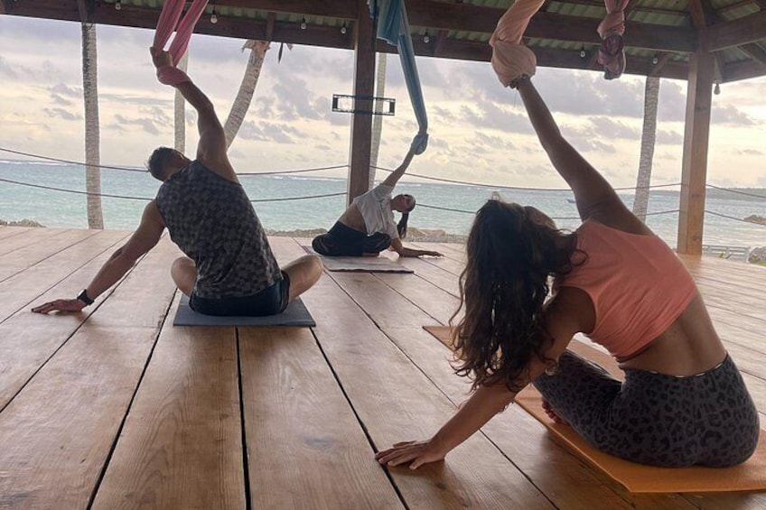 People practicing yoga on wooden mats under a wooden structure by the sea. 2