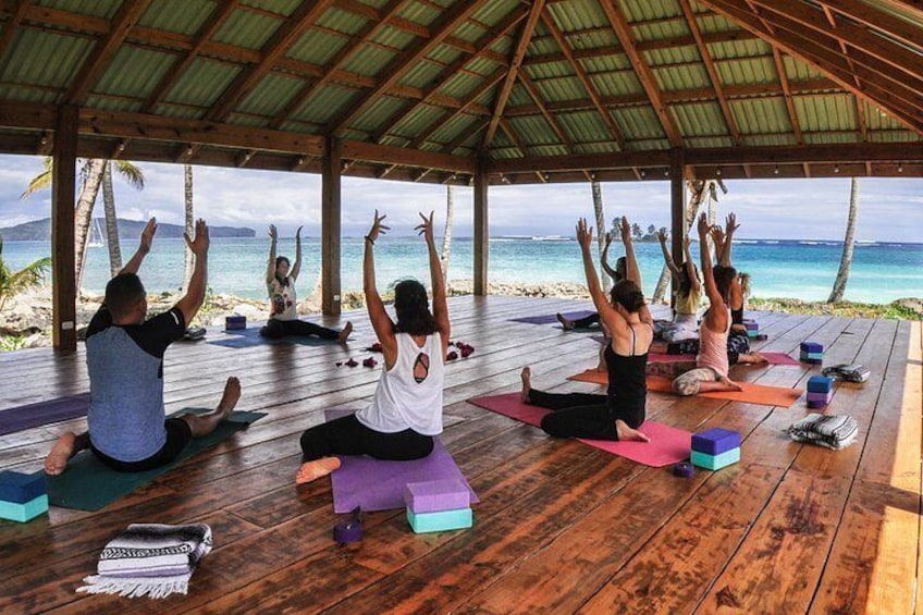A group of people practicing yoga on wooden mats under a wooden shelter by the beach. 4